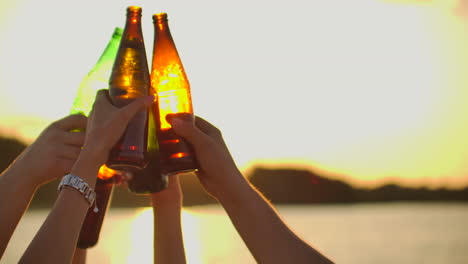 Teenagers-are-dancing-with-hands-up-and-clink-beer-from-glass-colorful-bottles.-This-is-perfect-party-at-sunset-on-the-lake-coast.